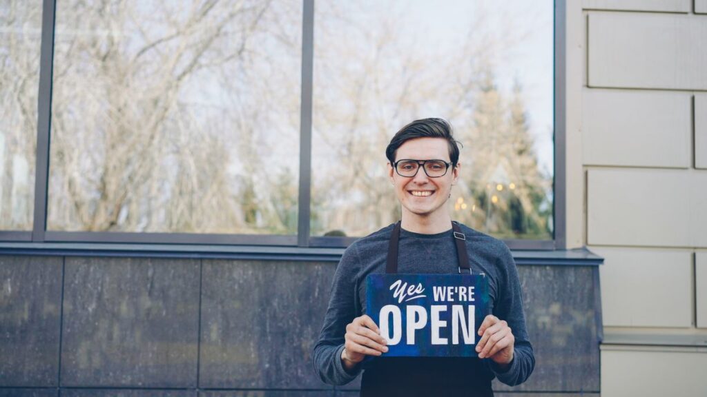 Smiling small business owner holding a Yes We’re Open sign